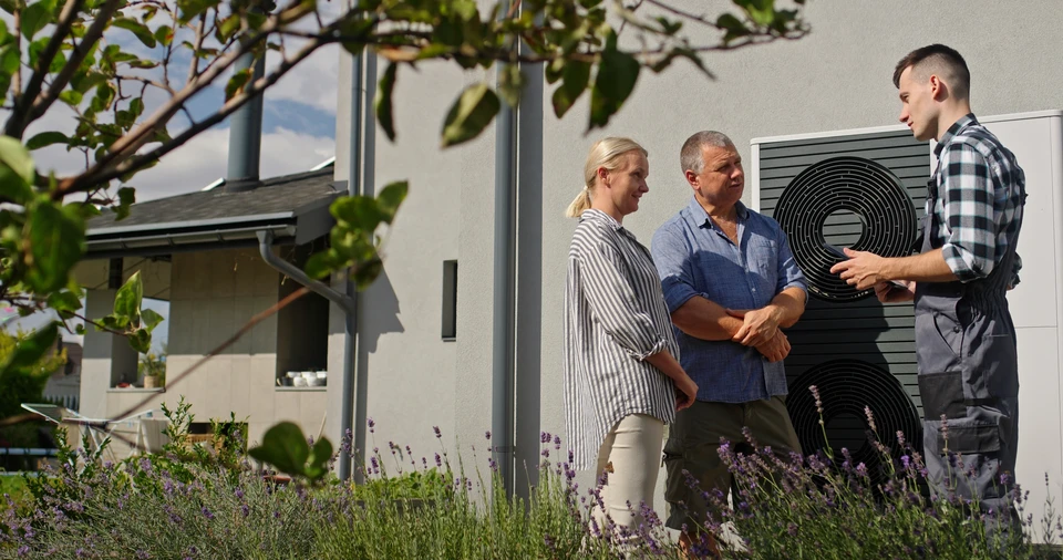 Scène extérieure devant maison moderne avec deux professionnels discutant près d'une unité de climatisation